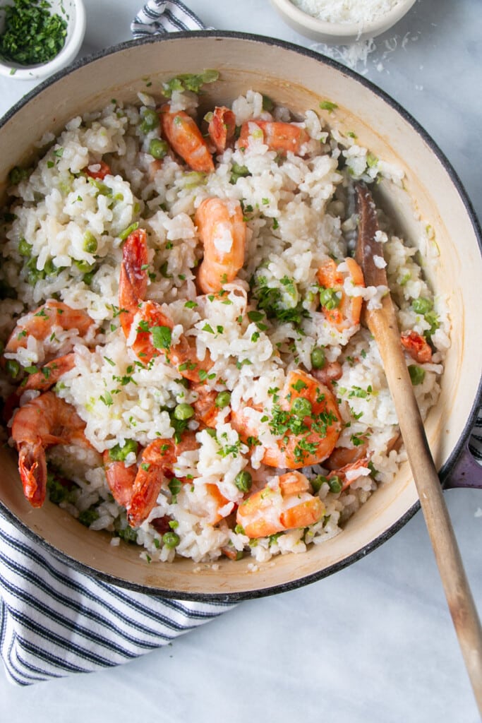 Oven Baked Risotto with bright pink cooked tiger prawns and peas in a large dutch oven. 