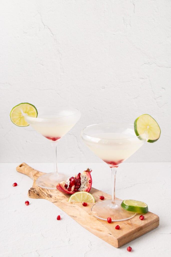 Lime Gimlet with a lime slice on the rim of a chilled martini glass and pomegranate seeds at the bottom of the glass.