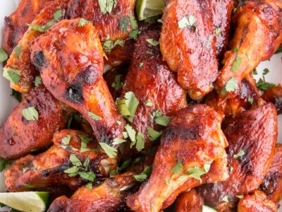 Gochujang Hot Wings in a pile with lime wedges and chopped cilantro garnish