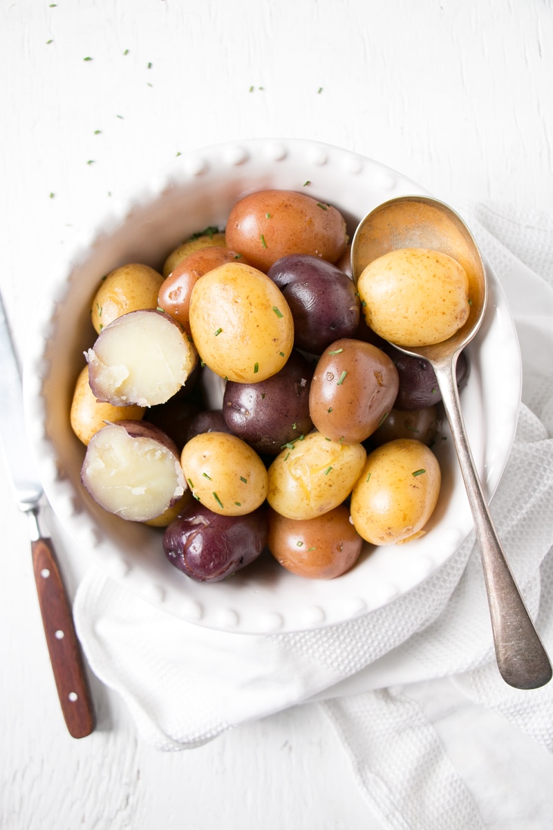 Bright trio coloured boiled potatoes with one cut in half showing a tender fluffy inside.