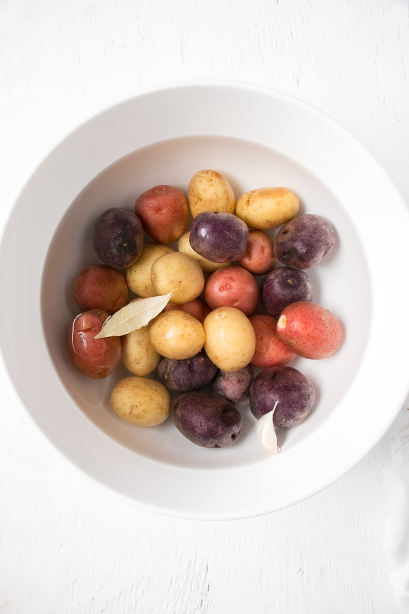 Jewelled coloured little potatoes covered with water in white bowl ready for microwave cooking. 