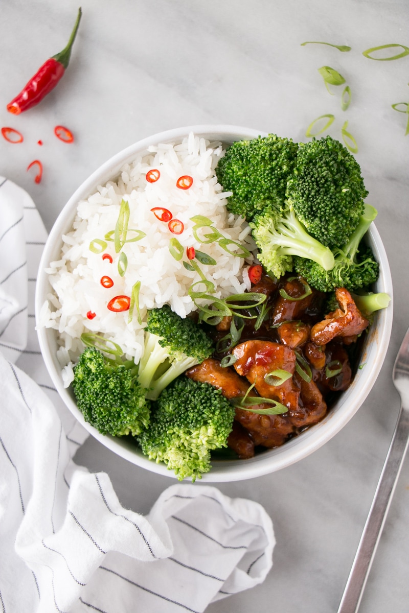 Steamed Broccoli in a shallow bowl with saucy chicken and fluffy white rice. 