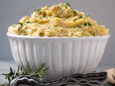 Creamy, piled high Holiday Make Ahead Mashed Potatoes in large white bowl with scattered parsley on top.