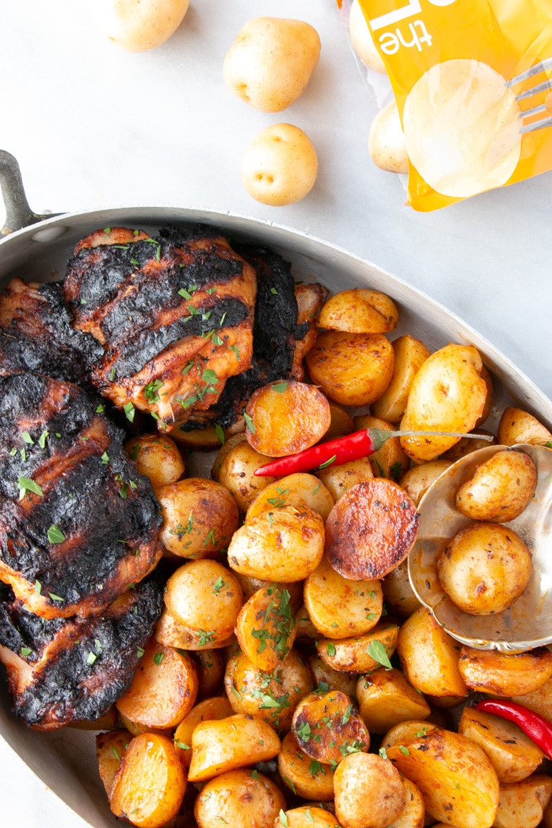 Grilled Peri Peri Chicken and Potatoes up close with some potatoes in a scalloped shaped serving spoon.