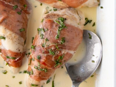 Prosciutto-Wrapped Chicken in a creamy mustard sauce with a scattering of fresh basil on top.