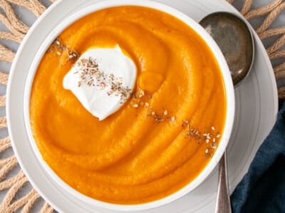 Thick deep orange roasted carrot soup in a white bowl with a big dollop of greek yogurt and an angled sprinkle of za'taar