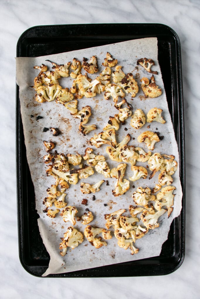 Charred tips roasted cauliflower on a parchment paper lined baking sheet. 