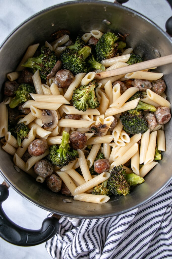 Roasted Sausage, Mushroom and Broccoli Pasta getting tossed together in a large metal pot. 