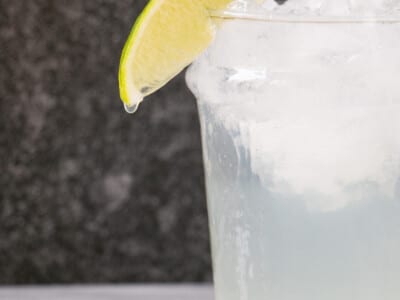 A tall glass with a dripping lime slice on the edge, have filled with crushed ice, tequila, lime juice and mineral water.
