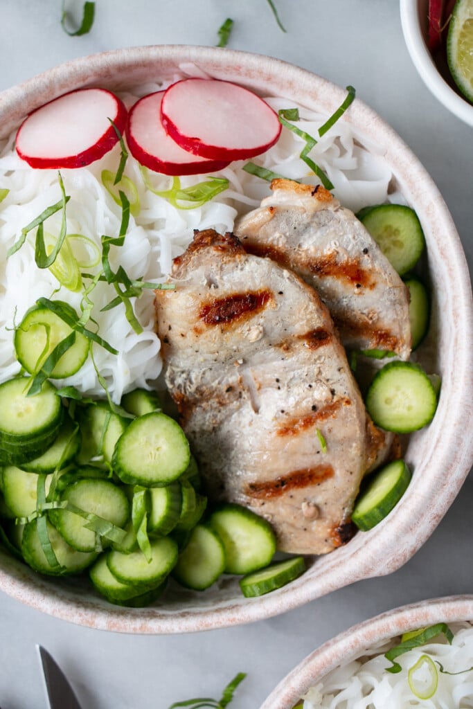 Vietnamese Noodle Bowls with grilled thin pork chops, sliced mini cucumbers, bright pink radishes, rice noodles and thinly sliced basil. 
