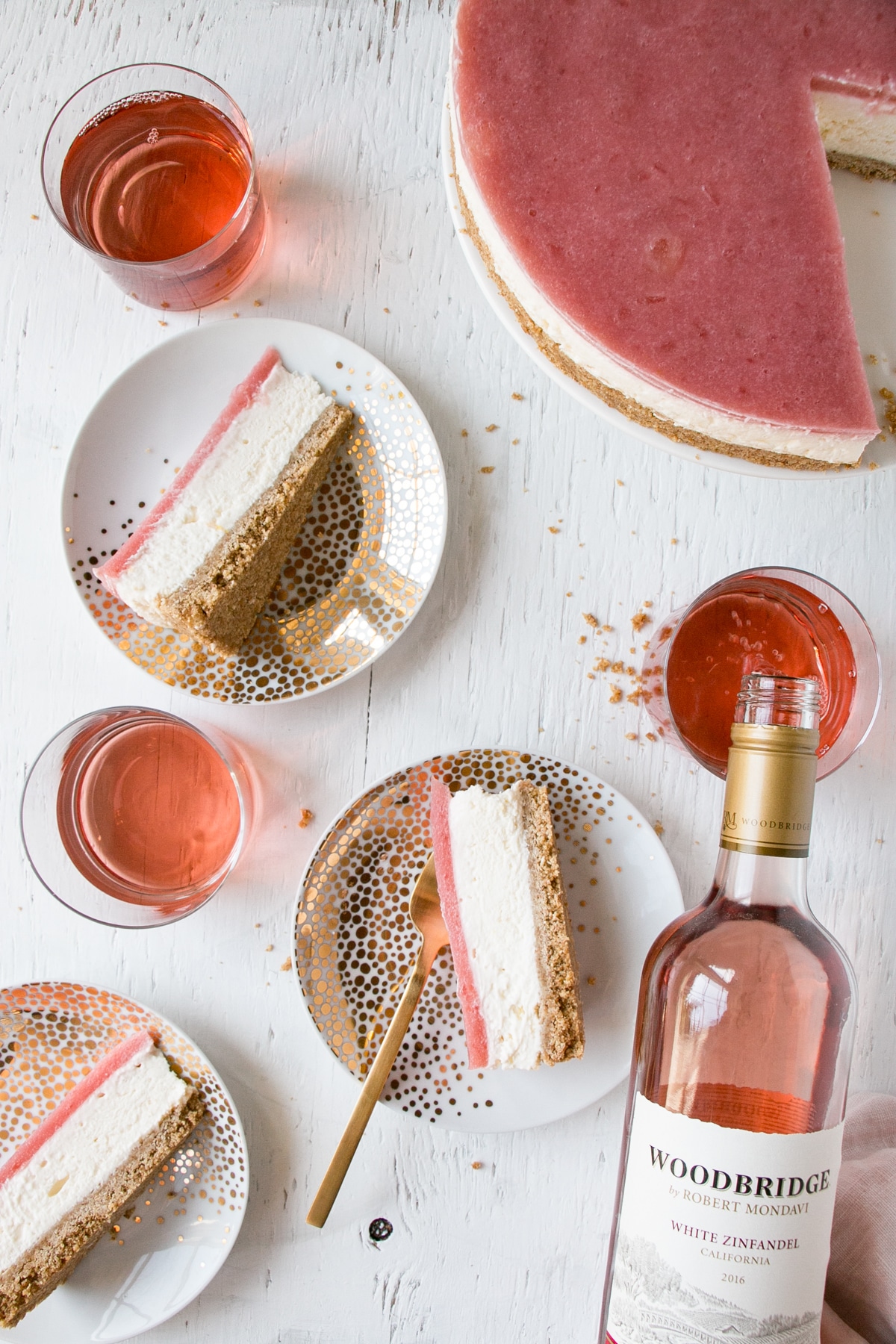 Slices of a No Bake Rhubarb Cheesecake on plates and glasses of rose wine.