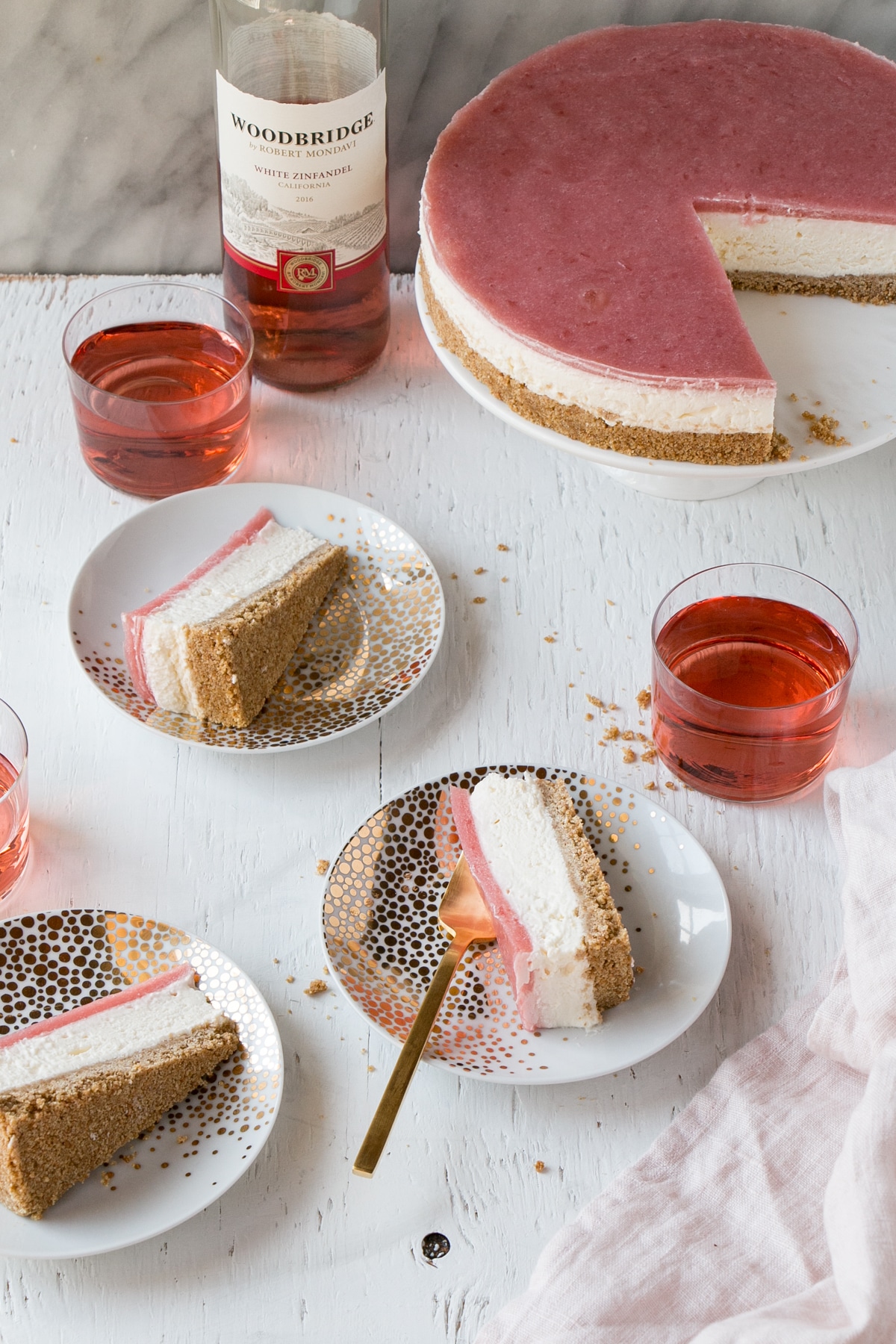 Slices of a No Bake Rhubarb Cheesecake on plates and glasses of rose wine.