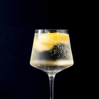 White wine spritzer in a tall wine glass with lemon rind in it.